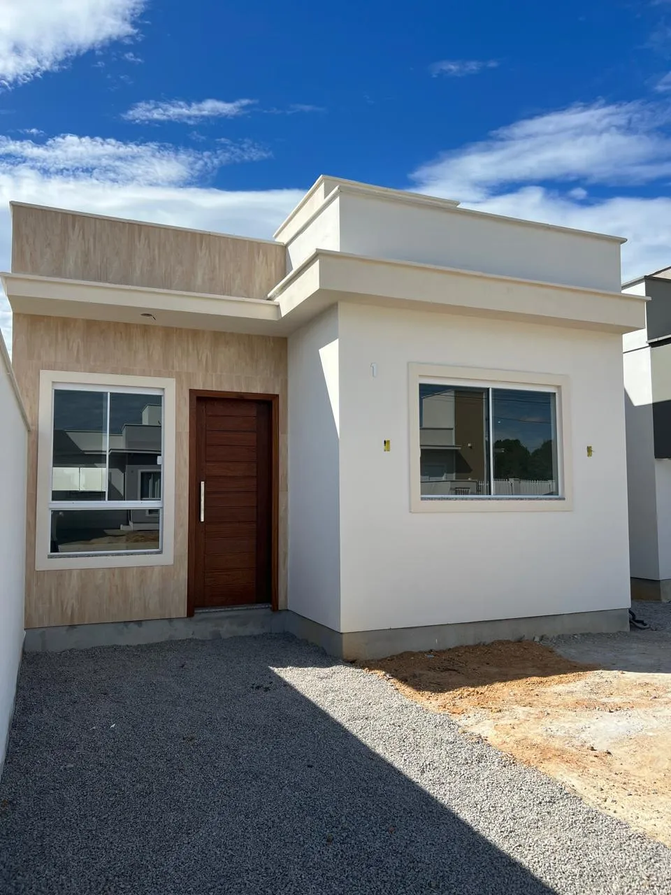 Fachada térrea da Casa Camélia, com revestimento de pedra clara e porta de madeira.